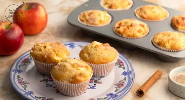 Frisch gebackene Apfelmuffins, die nach einem tollen apfelmuffins rezept duften. Daneben liegen Äpfel und Zimt.