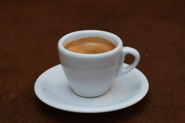 Ein kleiner weißer Becher mit cremigem, doppeltem Espresso, italienisch zubereitet, steht auf einer Untertasse.