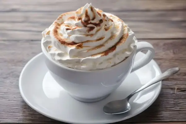 Ein cremiger Kapuziner Kaffee, üppig garniert mit Schlagsahne und Zimt, wartet auf einem Holztisch.