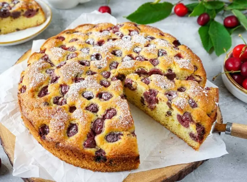 Ein saftiger Kirschkuchen mit Puderzucker bestreut, ein Stück herausgeschnitten.